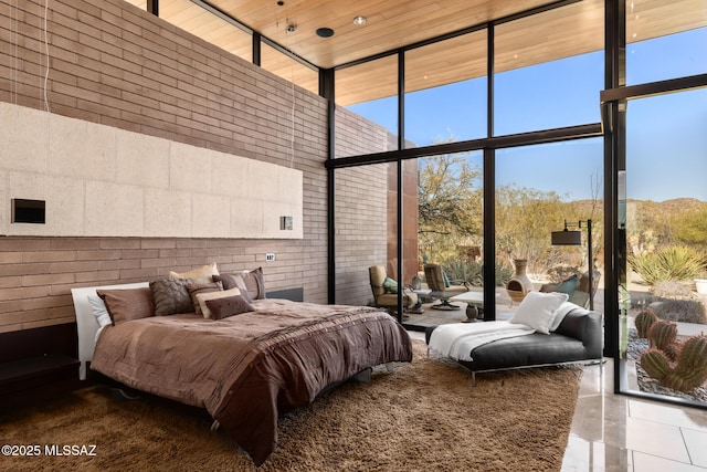 tiled bedroom with multiple windows, floor to ceiling windows, a high ceiling, and brick wall