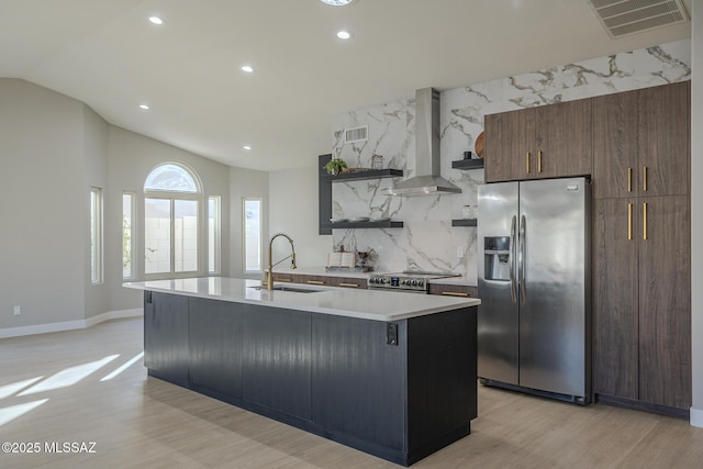 kitchen with appliances with stainless steel finishes, tasteful backsplash, a kitchen island with sink, wall chimney exhaust hood, and sink