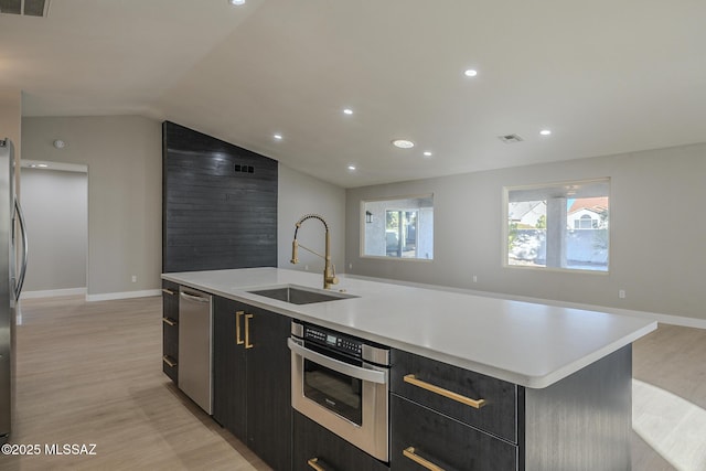 kitchen featuring lofted ceiling, light hardwood / wood-style floors, sink, an island with sink, and stainless steel appliances