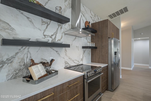 kitchen featuring light hardwood / wood-style floors, appliances with stainless steel finishes, backsplash, dark brown cabinets, and wall chimney range hood