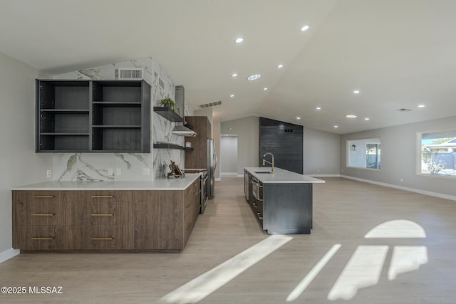 kitchen with lofted ceiling, tasteful backsplash, light hardwood / wood-style floors, sink, and an island with sink