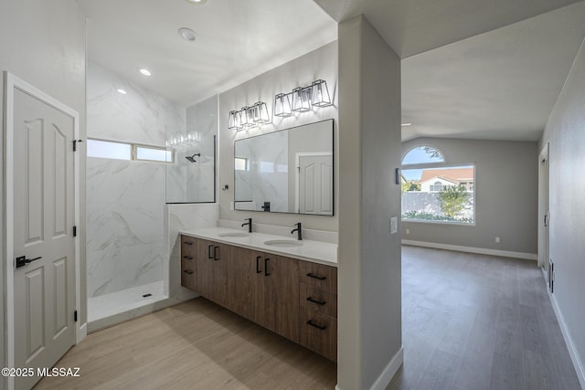 bathroom featuring wood-type flooring, vaulted ceiling, vanity, and a tile shower