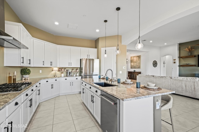 kitchen with stainless steel appliances, a sink, open floor plan, wall chimney range hood, and a center island with sink