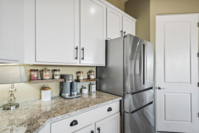 kitchen featuring freestanding refrigerator, light stone counters, and white cabinetry