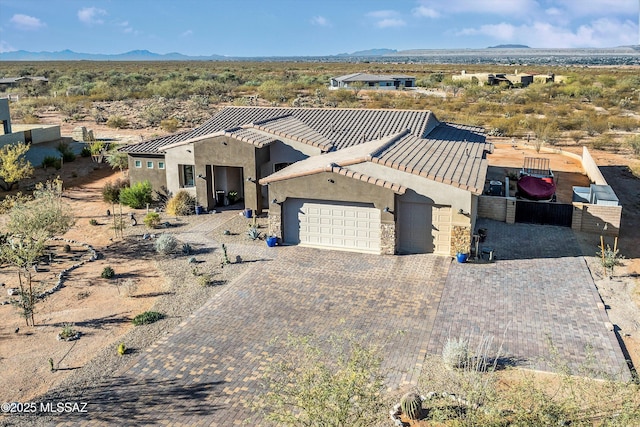 view of front facade with a mountain view, a garage, stone siding, decorative driveway, and stucco siding