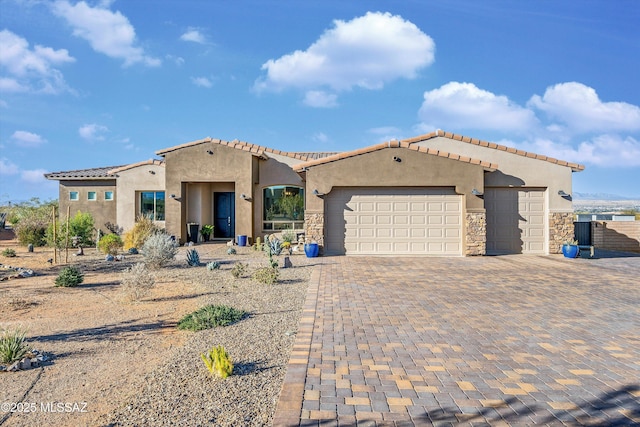 mediterranean / spanish home with decorative driveway, a tile roof, stucco siding, an attached garage, and stone siding