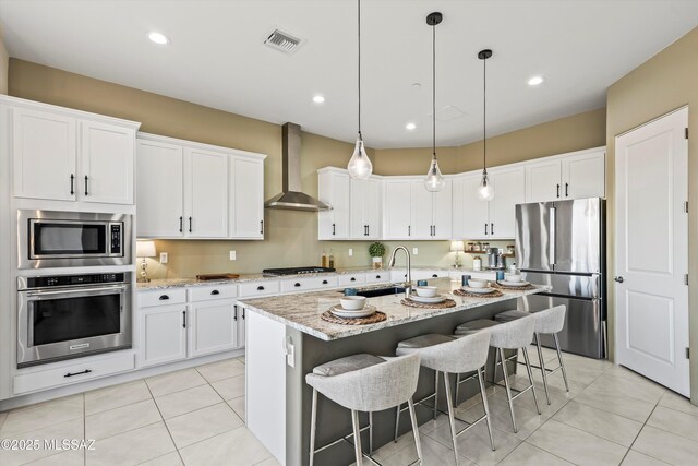 kitchen featuring sink, white cabinetry, appliances with stainless steel finishes, a kitchen island with sink, and wall chimney range hood