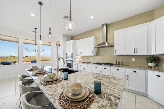 kitchen featuring wall chimney exhaust hood, a breakfast bar, sink, a center island with sink, and stainless steel appliances