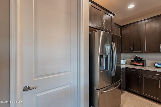 kitchen with dark brown cabinetry, stainless steel fridge with ice dispenser, light stone counters, and light tile patterned floors