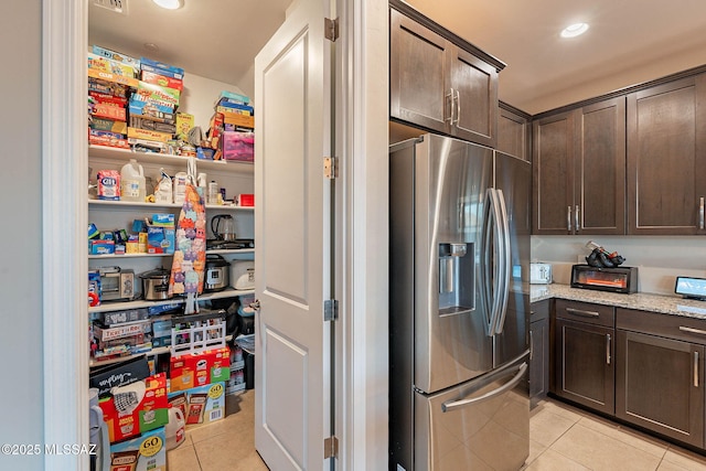 kitchen with light tile patterned flooring, light stone counters, dark brown cabinetry, and stainless steel fridge with ice dispenser