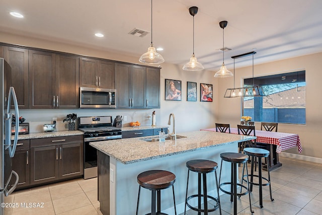 kitchen featuring dark brown cabinetry, sink, hanging light fixtures, stainless steel appliances, and a kitchen island with sink