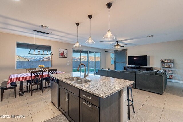 kitchen with decorative light fixtures, sink, light tile patterned floors, stainless steel dishwasher, and light stone counters