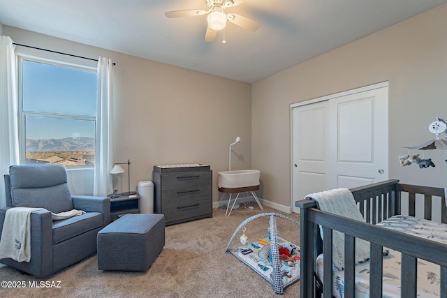 bedroom with a nursery area, ceiling fan, light colored carpet, and a closet