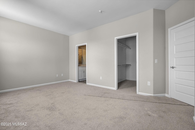 unfurnished bedroom with a walk in closet, ensuite bath, baseboards, and carpet floors