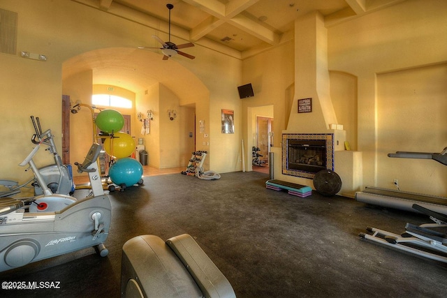 exercise area with a fireplace, a ceiling fan, arched walkways, and coffered ceiling