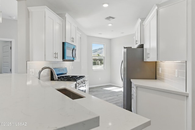 kitchen featuring light stone counters, stainless steel appliances, visible vents, and white cabinetry