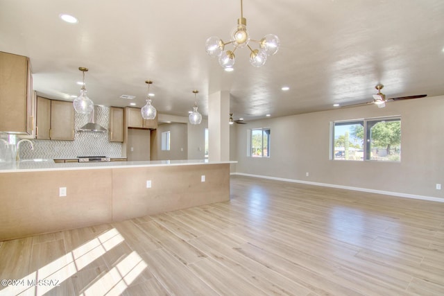 kitchen with wall chimney range hood, sink, light hardwood / wood-style flooring, hanging light fixtures, and light brown cabinetry