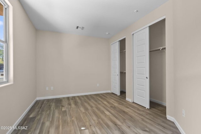 unfurnished bedroom with multiple closets and wood-type flooring