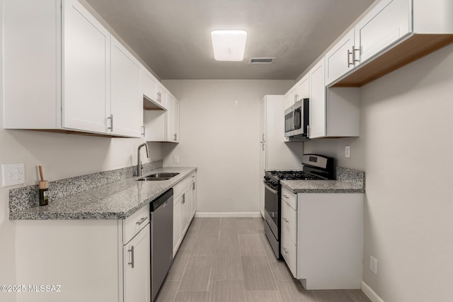 kitchen with light stone counters, sink, white cabinets, and appliances with stainless steel finishes