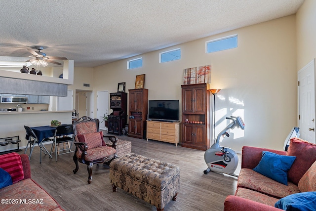 living room featuring a towering ceiling, ceiling fan, visible vents, and wood finished floors