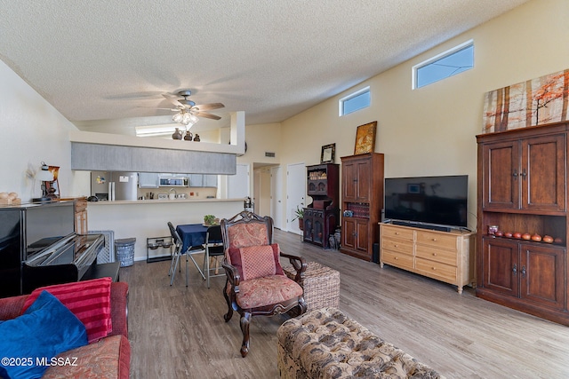 living area featuring ceiling fan, high vaulted ceiling, a textured ceiling, wood finished floors, and visible vents