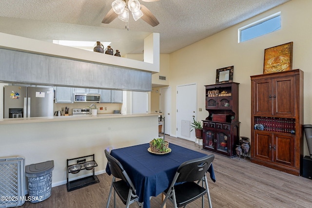 dining room with light wood finished floors, visible vents, lofted ceiling, ceiling fan, and a textured ceiling