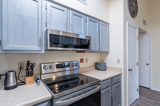 kitchen featuring stainless steel appliances, wood finished floors, light countertops, and visible vents