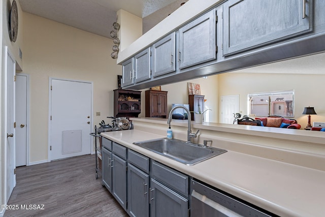 kitchen featuring gray cabinetry, dark wood-type flooring, a sink, light countertops, and stainless steel dishwasher