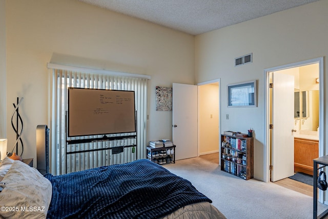 carpeted bedroom featuring visible vents, ensuite bath, a textured ceiling, and a towering ceiling