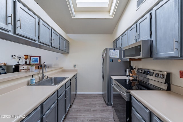 kitchen with light wood finished floors, baseboards, stainless steel appliances, light countertops, and a sink