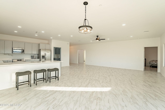 kitchen featuring decorative light fixtures, a kitchen bar, stainless steel appliances, ceiling fan, and gray cabinetry