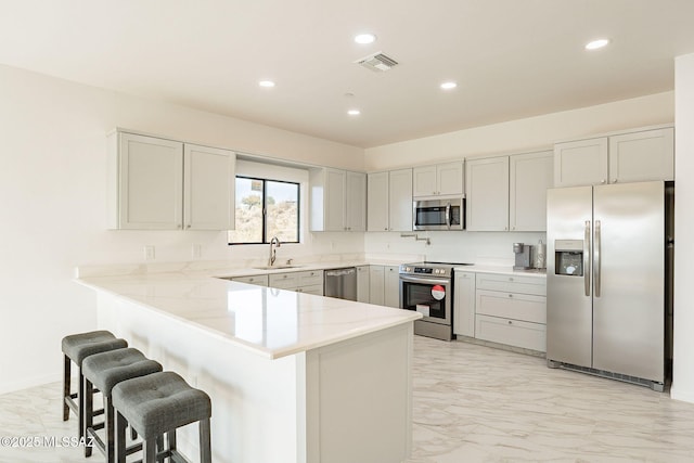 kitchen with a kitchen breakfast bar, appliances with stainless steel finishes, kitchen peninsula, and sink