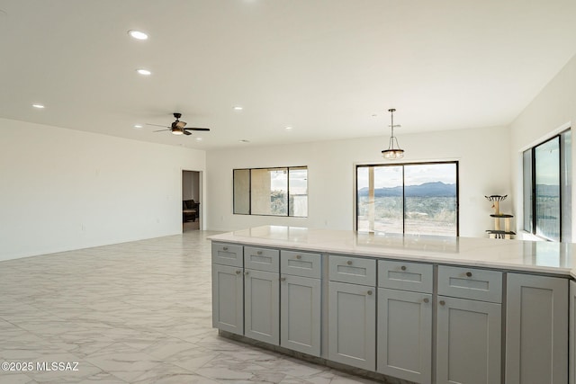 kitchen with ceiling fan, light stone countertops, hanging light fixtures, and gray cabinetry