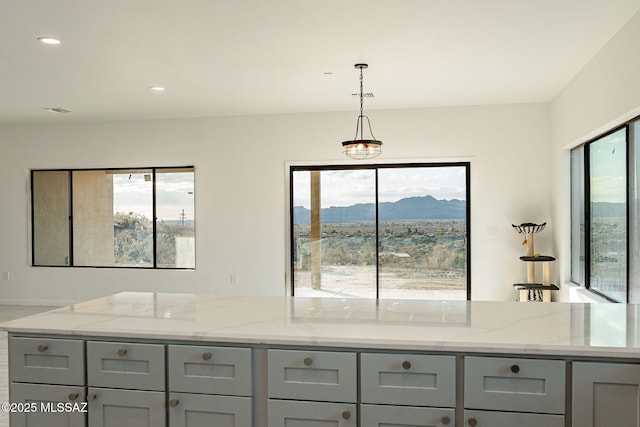 kitchen featuring a mountain view, light stone counters, gray cabinets, and hanging light fixtures