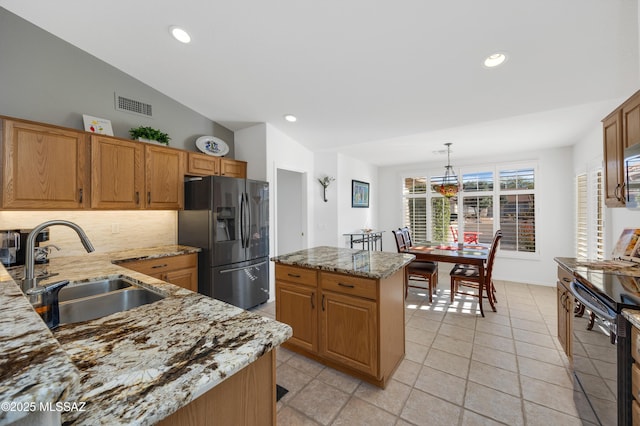 kitchen featuring hanging light fixtures, a kitchen island, black appliances, light stone counters, and sink