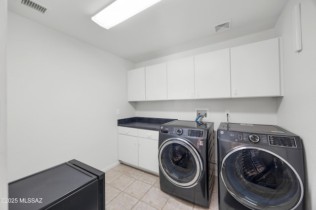 clothes washing area featuring washing machine and dryer, cabinets, and light tile patterned floors