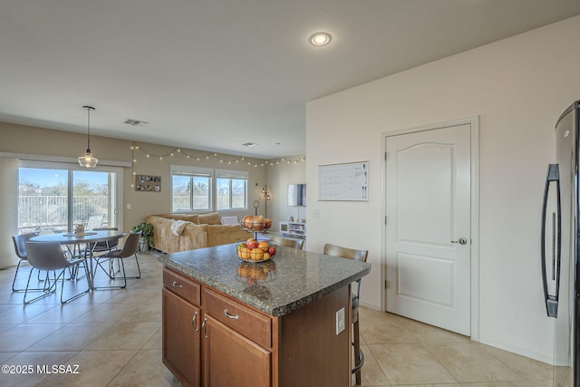 kitchen featuring stainless steel refrigerator, dark stone countertops, hanging light fixtures, a center island, and light tile patterned flooring