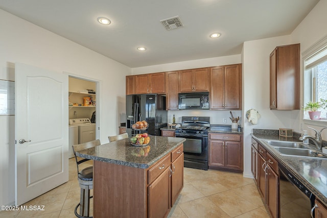 kitchen featuring washer and dryer, a breakfast bar, sink, a center island, and black appliances