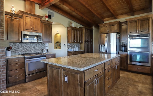 kitchen with backsplash, stainless steel appliances, a center island, lofted ceiling with beams, and light stone countertops