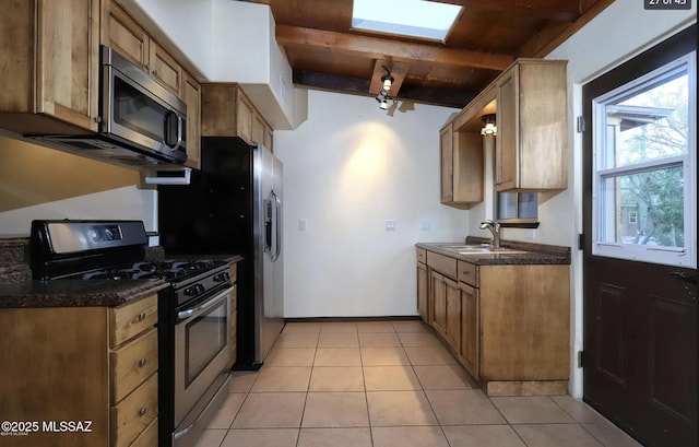 kitchen with sink, a skylight, dark stone counters, light tile patterned floors, and stainless steel appliances