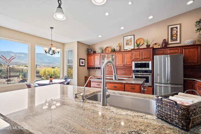 kitchen with sink, a center island with sink, appliances with stainless steel finishes, a mountain view, and pendant lighting