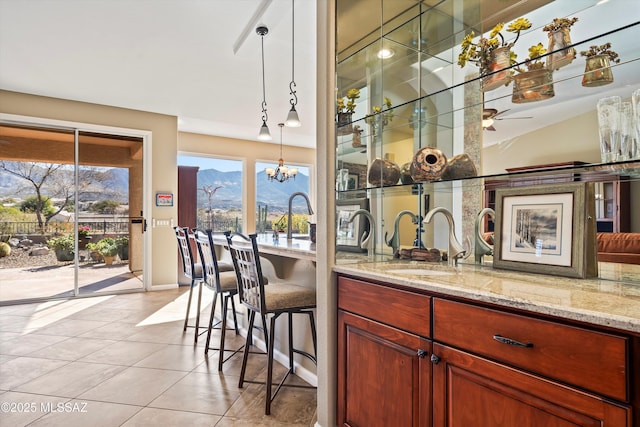 bar featuring pendant lighting, sink, light tile patterned floors, a mountain view, and light stone countertops