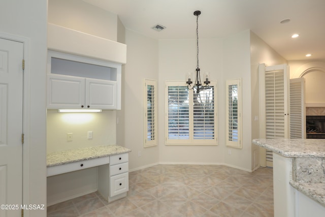 kitchen featuring built in desk, pendant lighting, white cabinets, and light stone counters