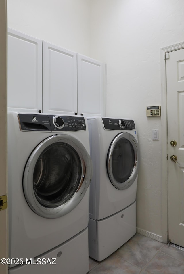 laundry area featuring separate washer and dryer, light tile patterned floors, and cabinets