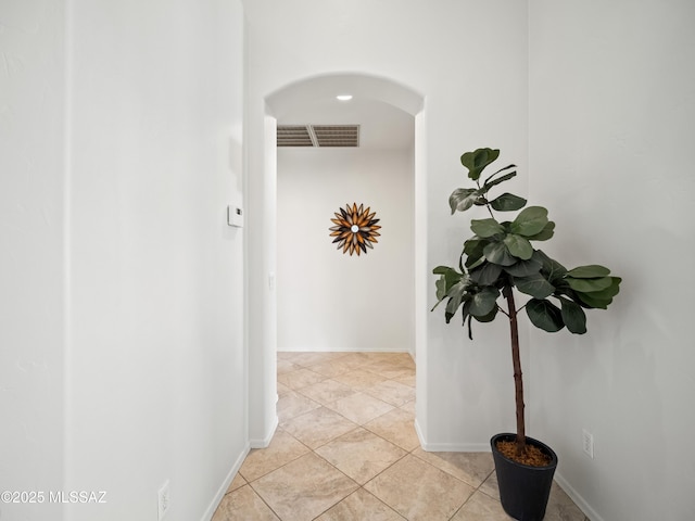 hallway with arched walkways, visible vents, baseboards, and light tile patterned floors