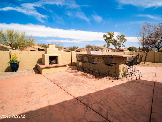 view of patio / terrace with a fenced backyard, an outdoor stone fireplace, and outdoor dry bar