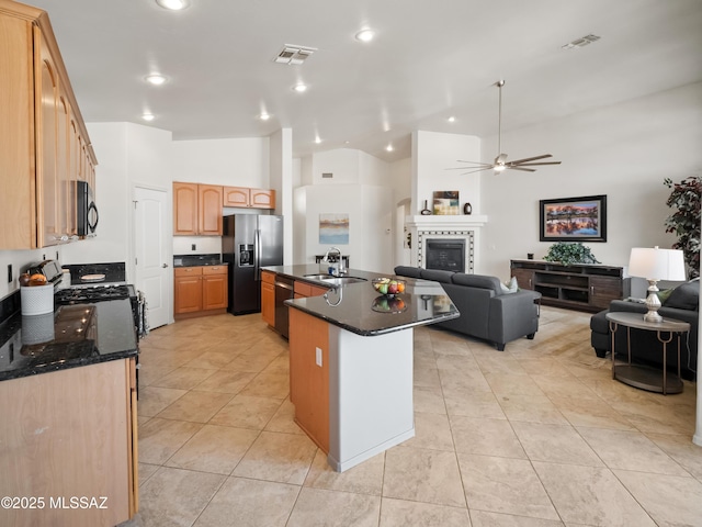 kitchen with a tile fireplace, a kitchen island with sink, a sink, open floor plan, and black appliances