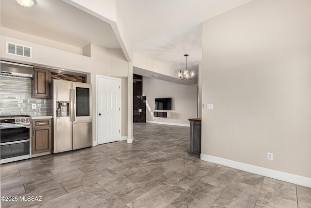 kitchen featuring stainless steel appliances, backsplash, a notable chandelier, wall chimney range hood, and pendant lighting