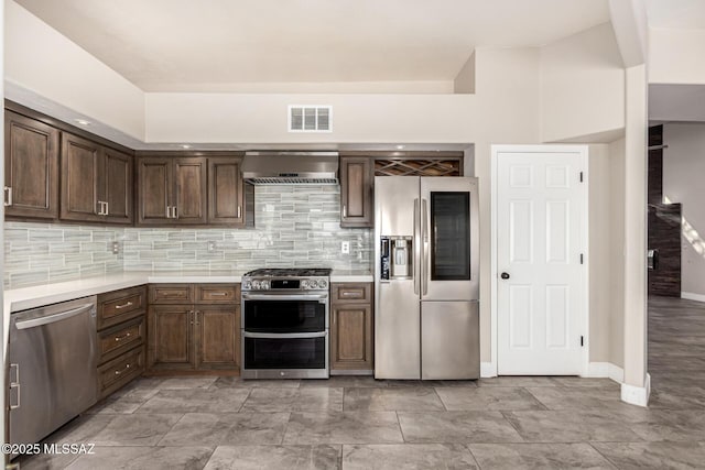 kitchen with dark brown cabinets, stainless steel appliances, wall chimney exhaust hood, and tasteful backsplash