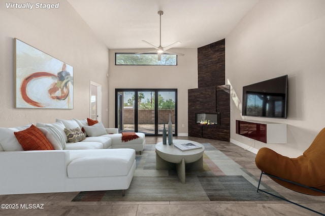 living room featuring ceiling fan, a high ceiling, and a stone fireplace